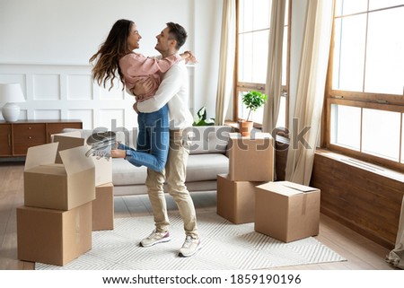 Happy couple arrive at bought house, cheerful husband lifts up on hands beloved wife family begin new life at first dwelling. Loan and mortgage, bank lending, delivered goods satisfied clients concept Royalty-Free Stock Photo #1859190196