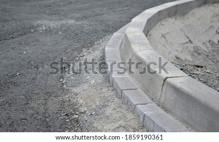 installation of concrete curb into concrete. in the space of the road, which so far has only a concrete base before laying the asphalt layer and rolling. Royalty-Free Stock Photo #1859190361