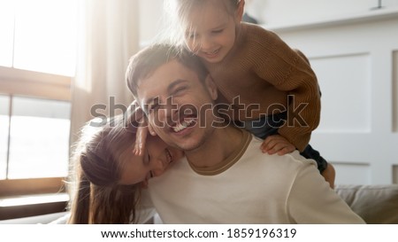 Two cheerful vivacious preschool daughters piggyback loving daddy laughing playing together in living room, close up image. Happy fatherhood and Father Day celebration, family bonding and love concept