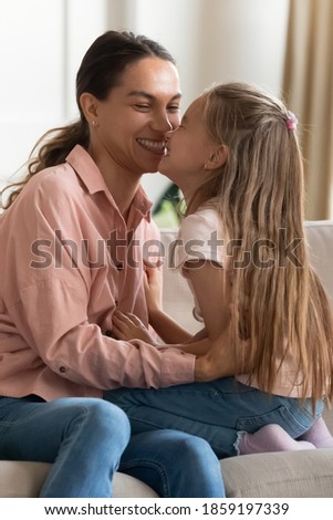 Young mum sit on sofa hug 6s daughter touch noses spend tender time together, parent enjoy communication with kid. Happy mother day celebration, trusting tender relationship of mom and child concept