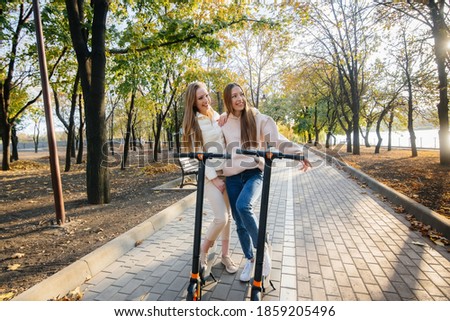 Two young beautiful girls ride electric scooters in the Park on a warm autumn day