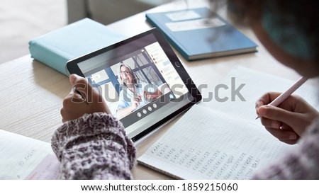 African american school kid child girl holding digital tablet talking to remote teacher tutor on social distance video conference call study online virtual class learning at home, over shoulder view. Royalty-Free Stock Photo #1859215060