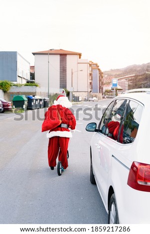 Back portrait of Santa Claus driving a children's scooter with big wheels to deliver the gifts because his car broke down