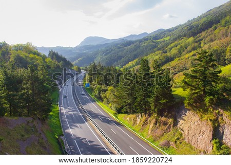 Highway in mountains with road sign and cars. Scenic curve road in autumn. Transport and traffic concept. Highway in valley, Basque country. Traffic way with beautiful landscape. Tourism in Europe.  Royalty-Free Stock Photo #1859220724