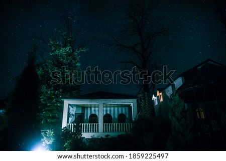 Old house with a Ghost in the forest at night or Abandoned Haunted Horror House. Old mystic building in dead tree forest. Surreal lights. Horror Halloween concept
