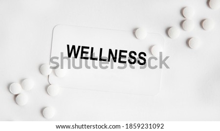On the card is the text of WELLNESS, next to the white tablets.