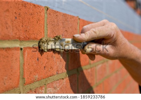 Close up of a brick wall and jointer trowel used by the worker to apply and level the mortar between bricks Royalty-Free Stock Photo #1859233786