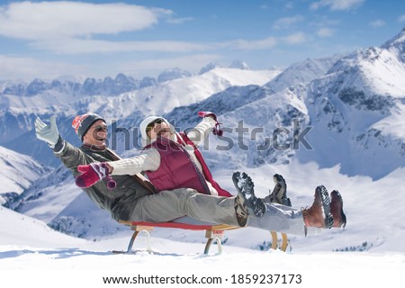 An Enthusiastic senior couple sledding down the slope with their arms outstretched on a snowy mountain