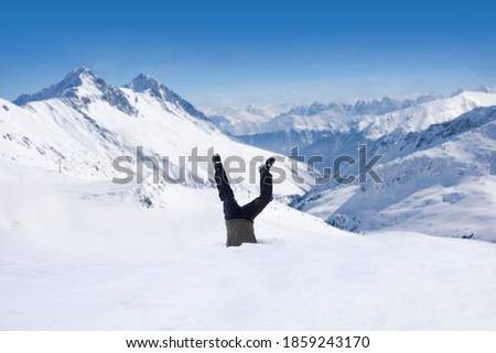 Man being in upside-down position inside a hole dug in the snow at the top of a remote mountain Royalty-Free Stock Photo #1859243170