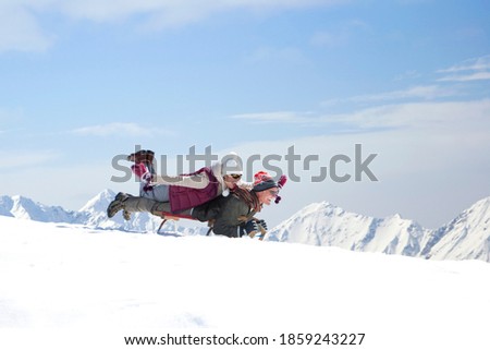 A side view of an adventurous senior couple lying on a sled together while sliding down the ski slope on a snowy mountain
