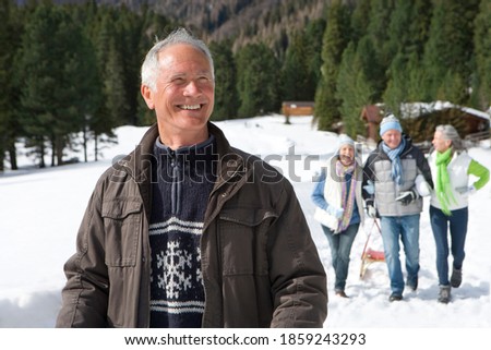 A smiling senior-adult man walking in the snowy woods with friends in the back ground