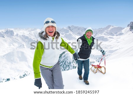 A happy and excited senior couple climbing up a snowy slope while pulling along a sled