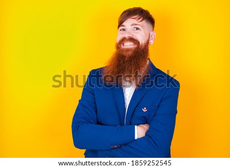 young red haired bearded Caucasian businessman standing against yellow background,  happy face smiling with crossed arms looking at the camera. Positive person.