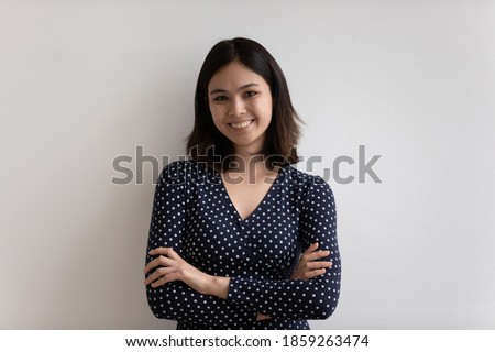 Head shot portrait smiling attractive Asian young woman with arms crossed standing on white studio background, successful entrepreneur businesswoman looking at camera, posing for photo