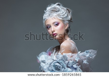 Winter Beauty Woman in clothes made of frozen flowers covered with frost, with snow on her face and shoulders. Christmas Girl Makeup. Make-up the snow Queen. Isolated on a gray background.