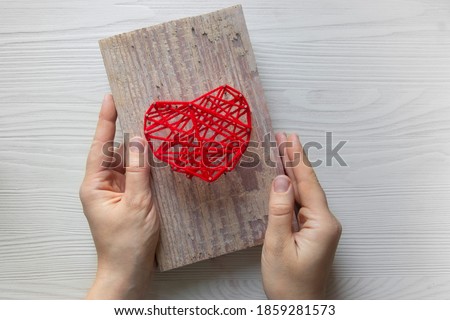 Step by step instruction: DIY gift for Valentine's Day. step 4: hands hold the finished pano picture with a heart made of threads and nails on a wooden board