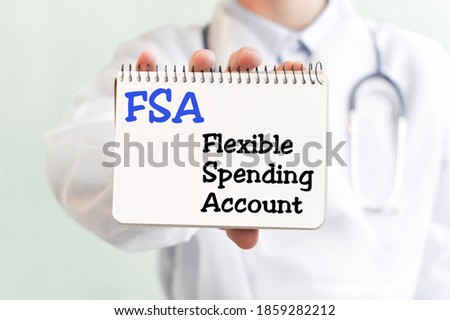 Doctor holding a card with text FSA Flexible Spending Account , medical concept. The text is written in blue letters in a medical journal. Royalty-Free Stock Photo #1859282212