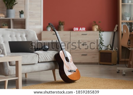 Background image of modern room interior with music instruments and On air sign, focus on guitar in foreground, copy space