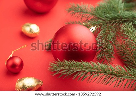 Christmas or New Year composition. Decorations, red balls, fir and spruce branches, on a red paper background. Side view, selective focus, close up.