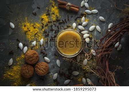 A jar of honey, pumpkin seeds, cookies, cinnamon sticks and a wreath of dry twigs and herbs. Composition on a black stone table sprinkled with bright spices. Top view