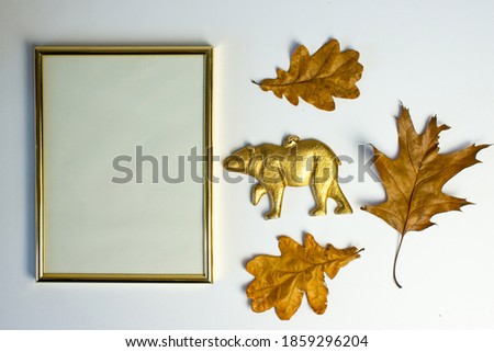 Empty gold frame with gold bear figurine on a white background among autumn leaves. Autumn background. Decoration. Sopy space. Gold bear christmas background.