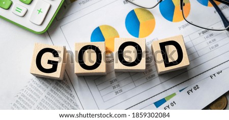 The inscription on the cubes, the word GOOD on the cubes of wooden texture. View from above. Desktop with documents. An inscription on a financial, business or economic theme.