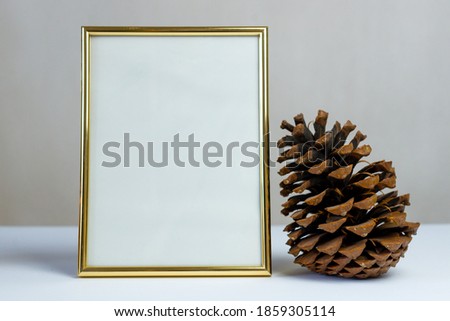 Empty gold picture frame on white background. Mock up frame. A large pine cone, a candle, autumn leaves. Autumn empty frame. Autumn background. Autumn composition. Cozy house. Copy space. Decoration.