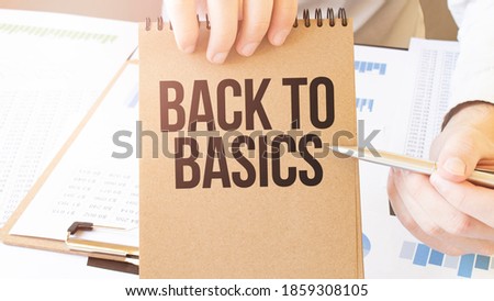 Text BACK TO BASICS on brown paper notepad in businessman hands on the table with diagram. Business concept