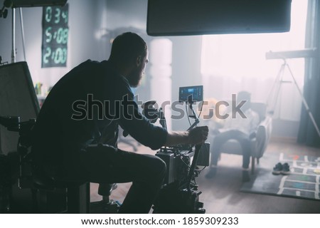 Director of photography with a camera in his hands on the set. Professional videographer at work on filming a movie, commercial or TV series. Filming process indoors, studio Royalty-Free Stock Photo #1859309233