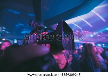 Director of photography with a camera in his hands on the set. Professional videographer at work on filming a movie, commercial or TV series. The filming process indoors, on a concert stage.