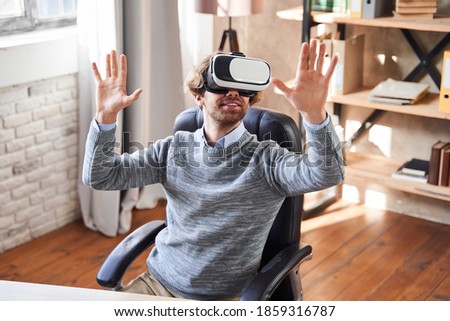 Low angle portrait of the happy amazed young man in virtual reality headset or 3d glasses at his workplace at home. Technology, virtual reality, cyberspace, entertainment and people concept