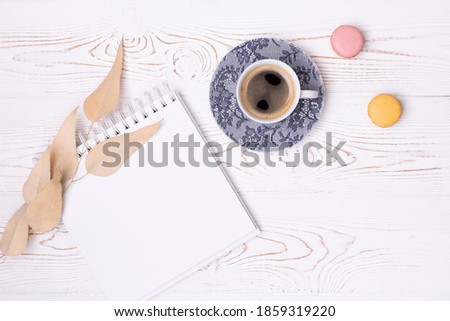 Composition from an empty diary with a spring, a cup of coffee and macaroons and beige leaves on a white shabby wooden table. Fashion flat lay