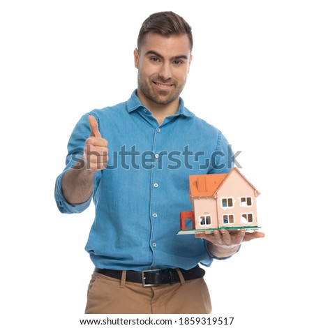 casual man giving a thumbs up while holding a house in his hand against white background