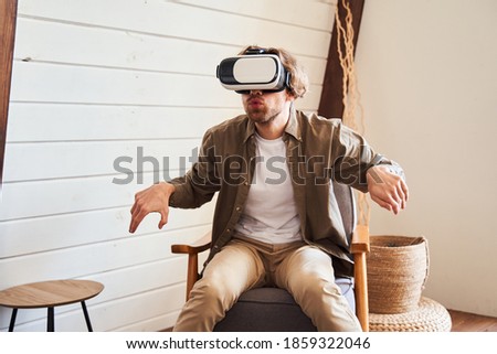 Attractive young man feeling real emotions while sitting at the armchair and playing at the virtual game, feeling expressed. Technology concept