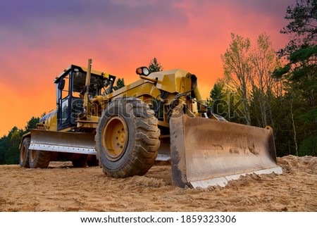 Motor Grader on road construction in forest area. Greyder leveling the sand, ground and gravel during road work. Heavy machinery and construction equipment for grading. Earthworks grader machine Royalty-Free Stock Photo #1859323306