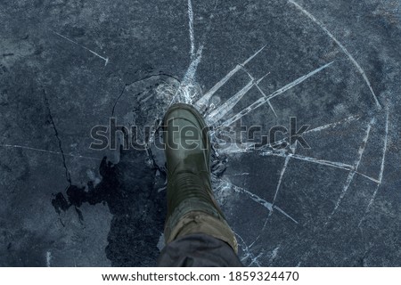Fisherman foot on broken cracked thin ice at lake. Dangerous fishing Royalty-Free Stock Photo #1859324470