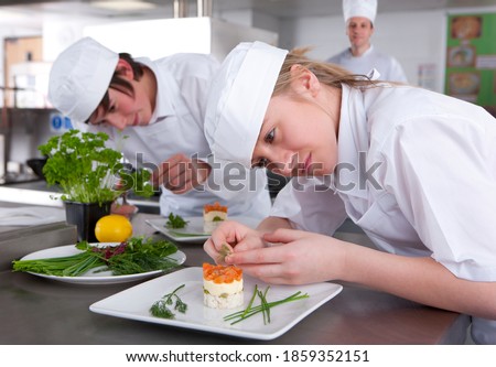 A close up shot of two young trainee chefs garnishing desert in a kitchen. Royalty-Free Stock Photo #1859352151