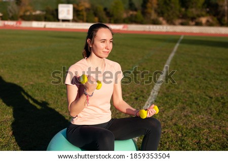 Woman sitting on fitball and doing exercises with dumbbells