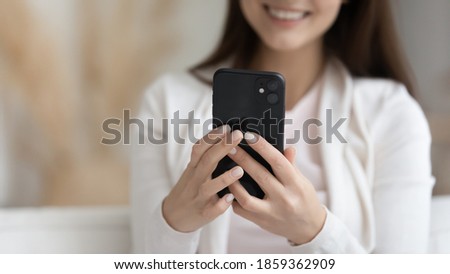 Must have attribute of everyday life. Close up cropped view of smiling young female posing indoors holding modern smartphone gadget in hands, making answering videocall, chatting shopping by internet