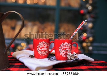 close up two red cups of coffee on table. Bakery exterior with Christmas decorations and fresh bread in showcase. Cozy outdoor bistro on Christmas eve. Copy space. seasonal greetings concepts