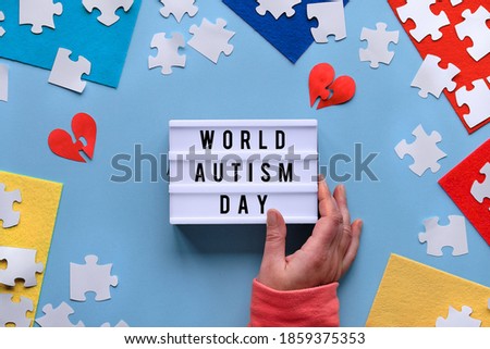 Hand hold lightbox, text World Autism Day. Creative design for April 2, Autism World Awareness day. Jigsaw puzzle element on layered felt pieces. Flat lay, top view, creative background..