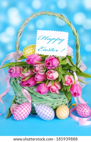 easter wicker basket with fresh pink tulips and eggs on blue background 