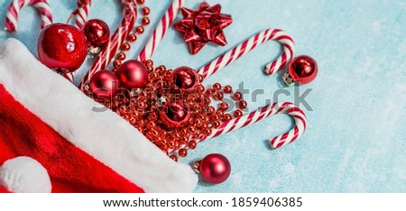 Banner. Christmas hat of Santa Claus, with Christmas candies, toys and sequins on a blue background. Minimal Christmas concept. Caramel cane. Copy of the text space.