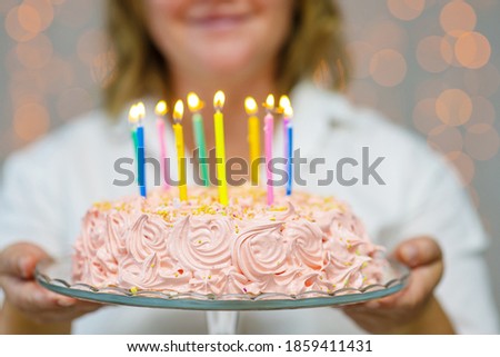 Young woman blowing out candles on a birthday cake over gray background.