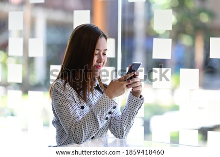 Image of a happy young beautiful woman is using mobile phone in modern office.