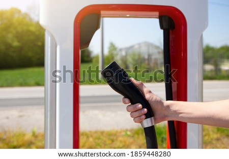A man holds a charger plug for an electric car Royalty-Free Stock Photo #1859448280