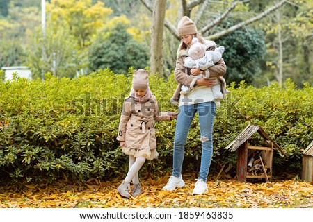 Happy family walking in autumnal park. Stylish young Caucasian Mother with kids. Autumn fashion. Fall season