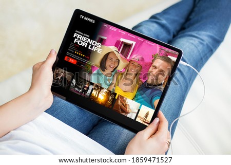 Woman watching TV series on tablet while sitting comfortably in sofa at home Royalty-Free Stock Photo #1859471527