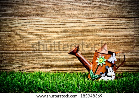 old and rusty watering can on green grass with wood background