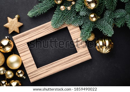 Christmas or New Year background with empty photo frame, fir tree and golden Christmas toys on black background